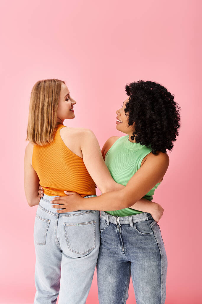 Twee divers vrouwen in gezellige casual kleding staan naast elkaar voor een roze achtergrond. - Foto, afbeelding