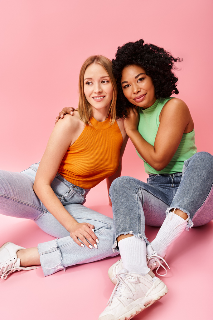 Two diverse women in casual attire sitting on the ground, striking a pose for a picture. - Photo, Image
