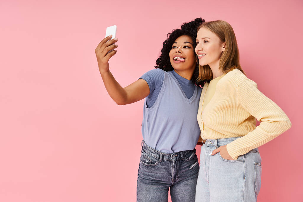 Deux jolies femmes diverses en tenue décontractée prenant un selfie avec un téléphone portable. - Photo, image