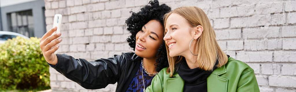 Deux jolies femmes diverses en tenue décontractée prenant un selfie avec un téléphone portable. - Photo, image