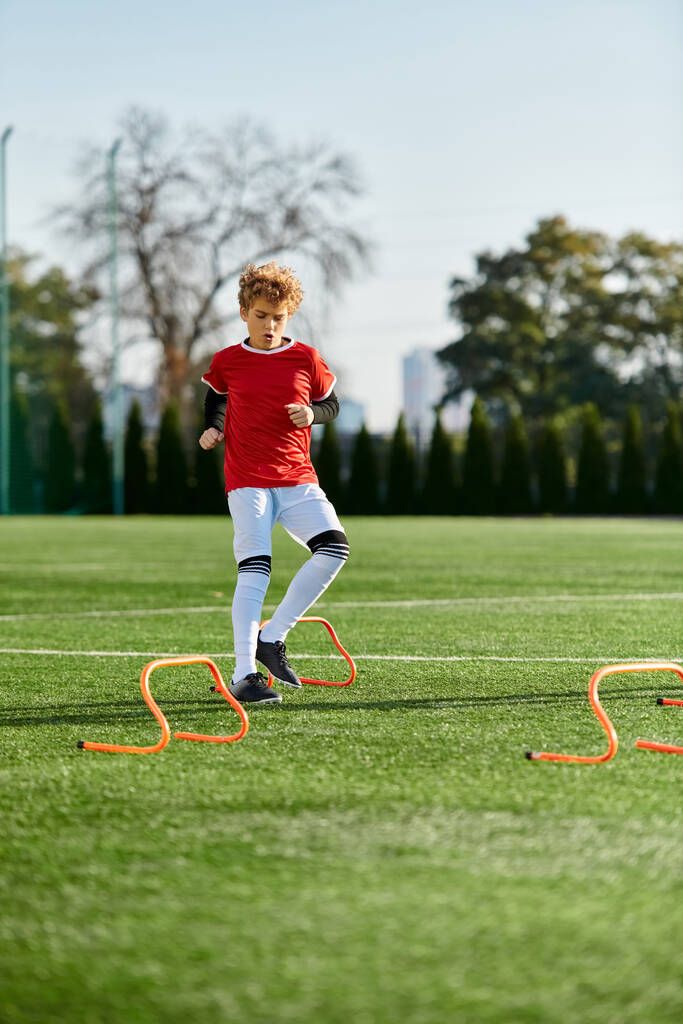 Een jonge jongen trapt energiek een voetbal op een veld, toont zijn ontluikende talent en passie voor de sport. De zon schijnt helder over zijn hoofd, wat zijn vastberaden gezicht en het levendige groene gras onder zijn voeten benadrukt.. - Foto, afbeelding