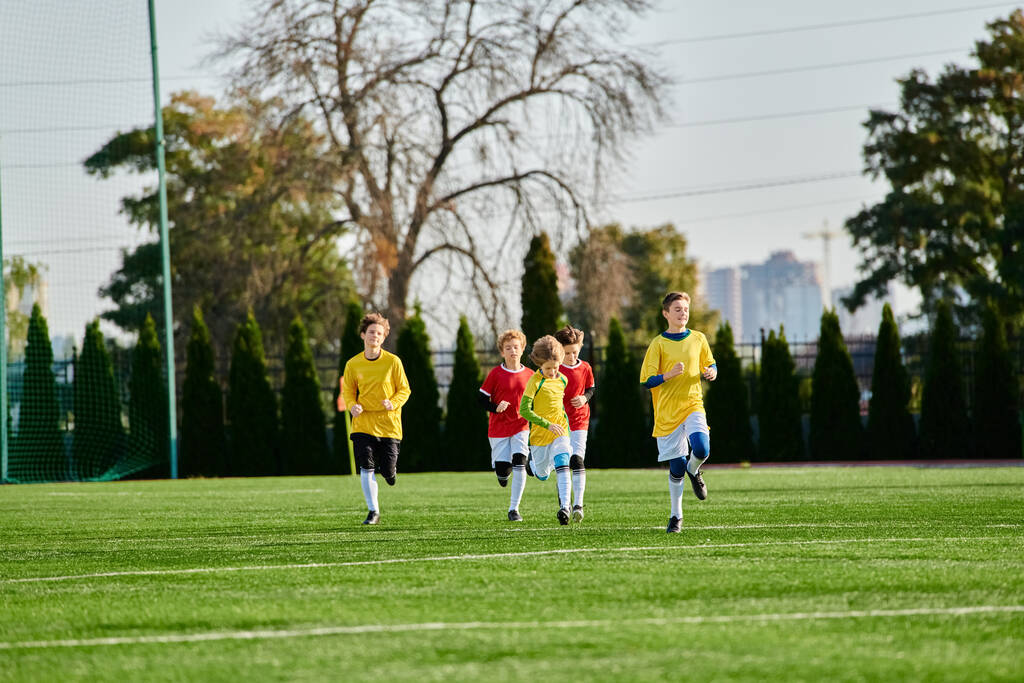 Grupa młodych chłopców energicznie gra w piłkę nożną na trawiastym polu, kopiąc piłkę w tę i z powrotem, śmiejąc się i dopingując się nawzajem.. - Zdjęcie, obraz
