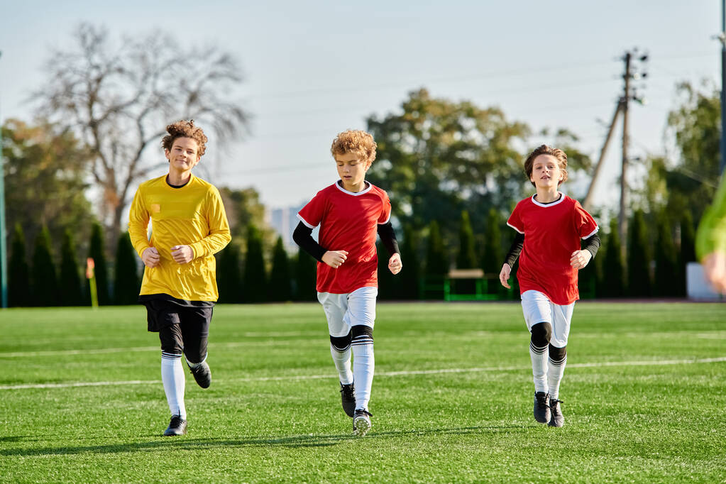 Żywa grupa młodych chłopców, ubranych w strój piłkarski, przemierza zadbane zielone boisko piłkarskie z determinacją i ekscytacją. - Zdjęcie, obraz