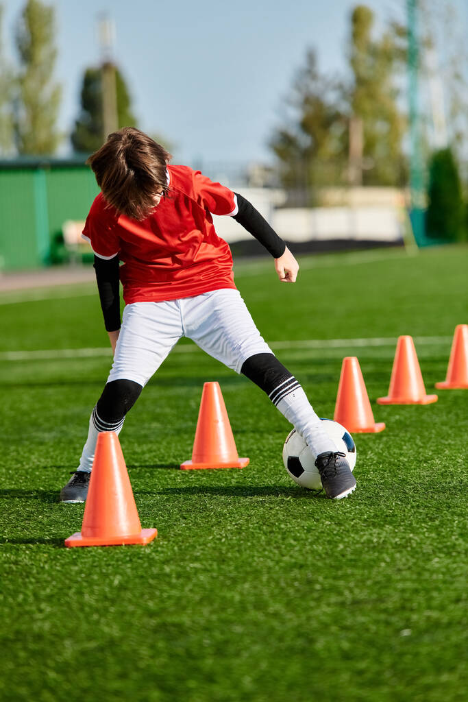 Een getalenteerde jongeman manoeuvreert vakkundig een voetbal rond levendige oranje kegels op een veld, toont zijn lenigheid en precisie in dribbelen en schoppen. - Foto, afbeelding