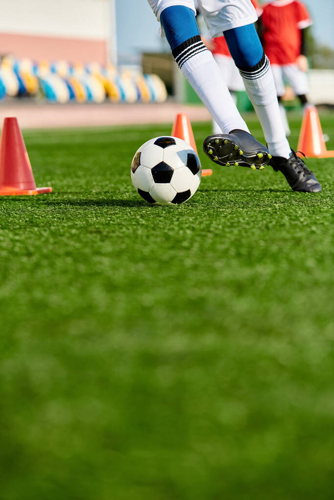 Osoba v atletické výstroji kopne fotbalový míček na zeleném poli pod jasně modrou oblohou za slunečného dne. - Fotografie, Obrázek