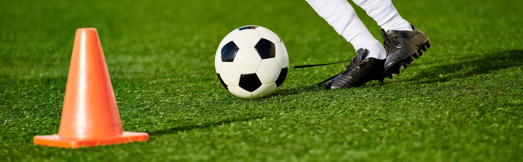 Una persona demuestra sus habilidades futbolísticas pateando una pelota de fútbol alrededor de un cono colocado en un campo. El jugador muestra precisión y agilidad en la maniobra de la pelota alrededor del obstáculo. - Foto, Imagen