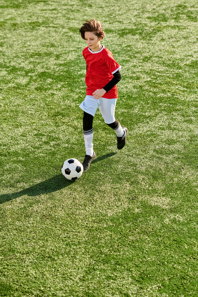 Ein kleiner Junge kickt mit Entschlossenheit und Geschick einen Fußball auf einer grünen Wiese und zeigt seine Leidenschaft für diesen Sport. - Foto, Bild