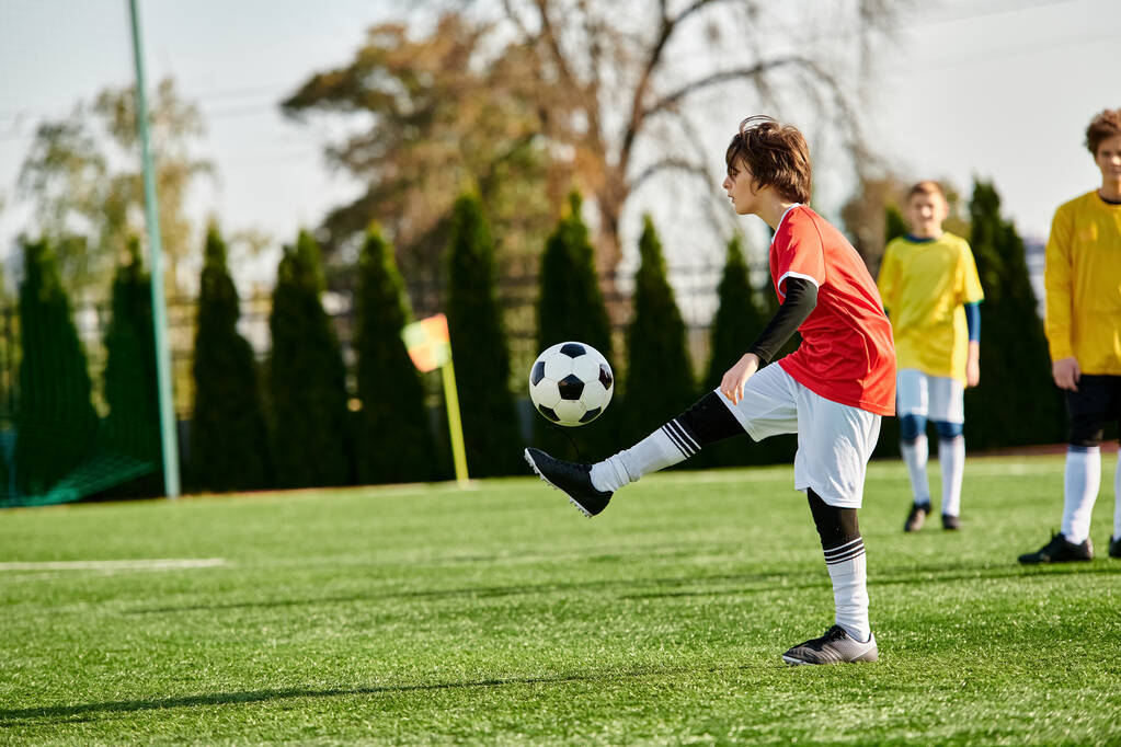 Młody chłopiec z determinacją kopie piłkę nożną na bujnym zielonym polu, pokazując swoją pasję i umiejętności dla sportu. - Zdjęcie, obraz