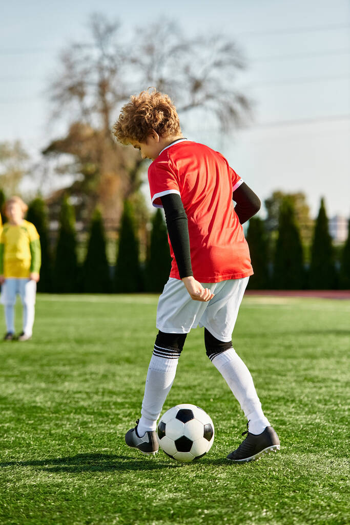 Un jeune garçon avec une expression déterminée donne un coup de pied à un ballon de football sur un terrain vert luxuriant sous le soleil, montrant sa passion pour le jeu. - Photo, image