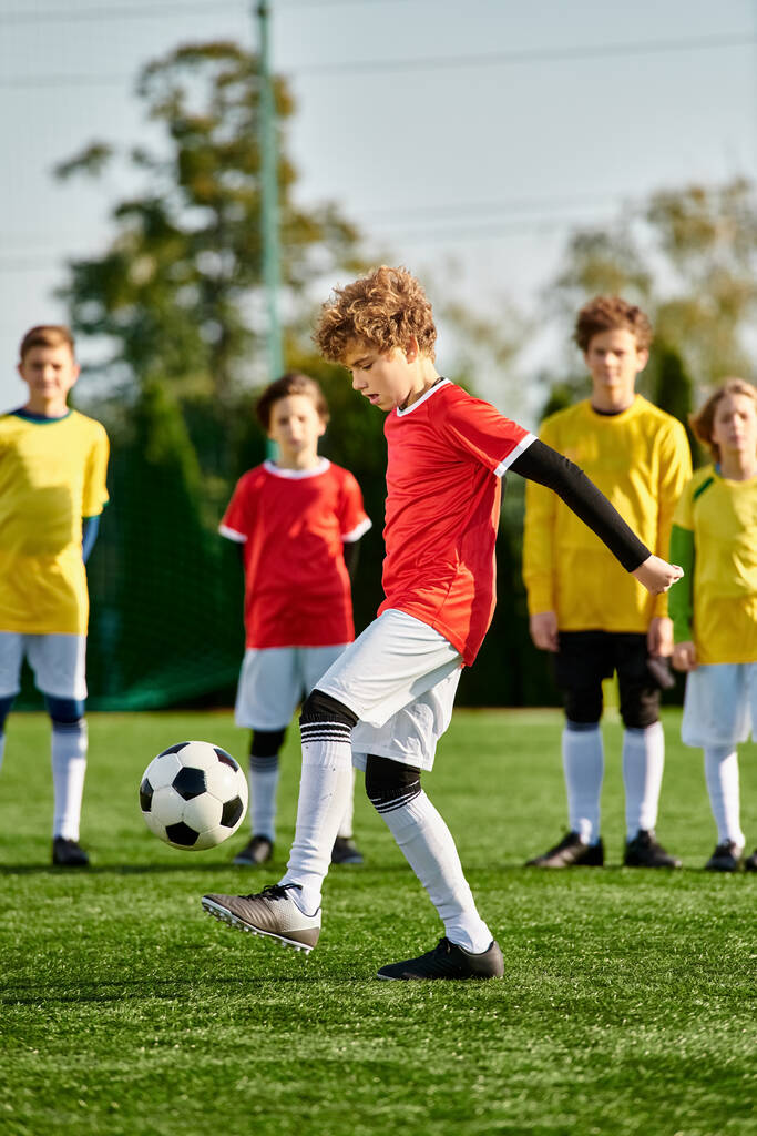 Een jonge jongen schopt energiek een voetbal over een uitgestrekt groen veld. De felle zon werpt lange schaduwen als hij vakkundig manoeuvreren de bal, waaruit blijkt vastberadenheid en passie voor de sport. - Foto, afbeelding