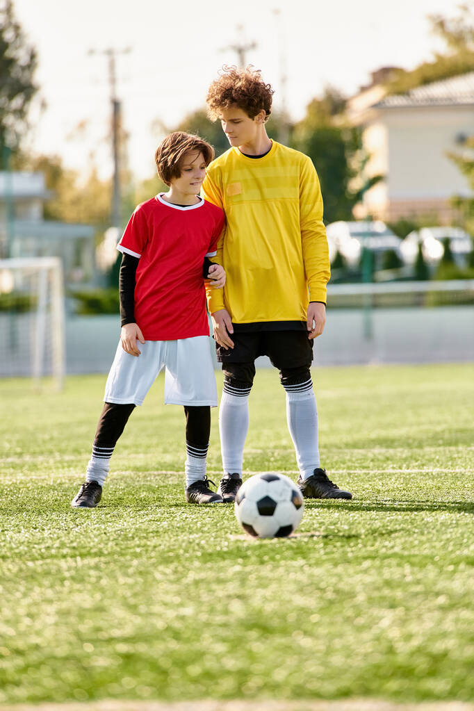 Двое молодых людей уверенно стоят на вершине футбольного поля, осматривая ландшафт под ними. Живая зеленая трава дополняет их энергичные позы, демонстрируя их любовь к красивой игре. - Фото, изображение
