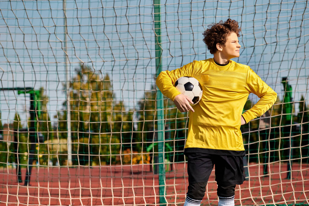 Muž v zářivé žluté košili sebevědomě drží fotbalový míč, předvádí svou vášeň pro sport. - Fotografie, Obrázek
