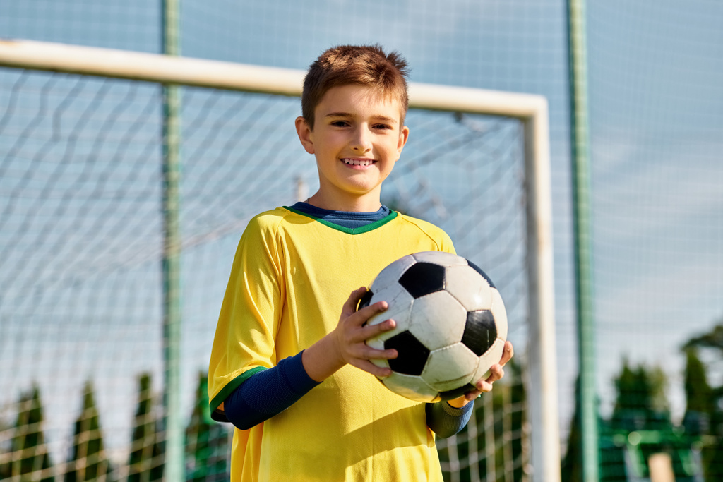 Nuori poika, päättäväinen ja keskittynyt, pitää jalkapalloa maalin edessä, valmiina ampumaan tarkasti ja taidokkaasti.. - Valokuva, kuva