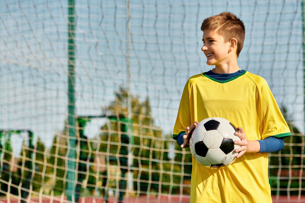 若い男の子は自信を持ってゴールの前に立って,サッカーボールを手にし,彼の勝利を想定しています. 彼の視線は網に固定されており,彼の目には決意がある.. - 写真・画像