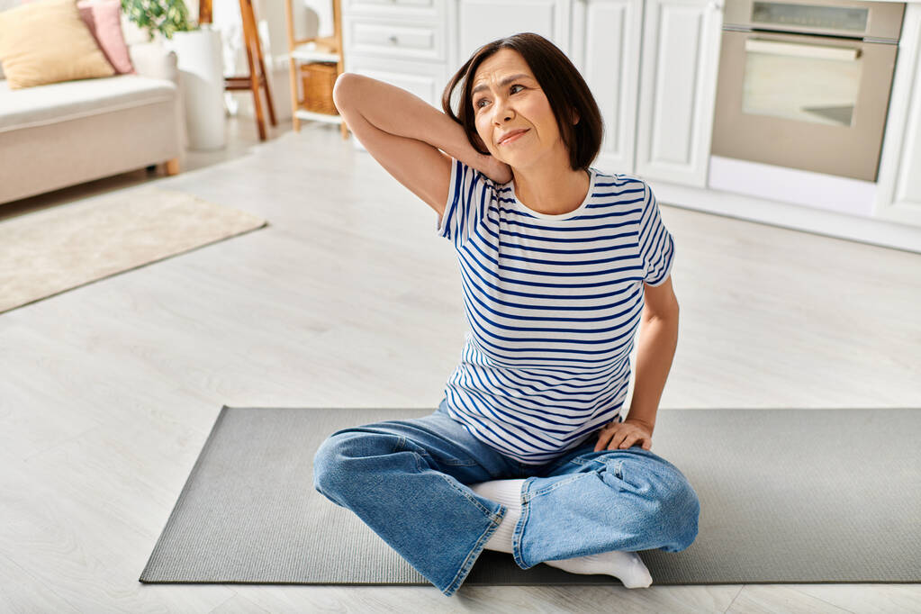 Mujer madura en ropa de casa acogedora practicando yoga en una estera en su sala de estar. - Foto, imagen