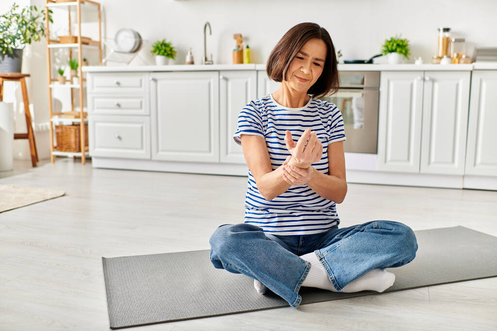 Una mujer hermosa madura en ropa cómoda practica yoga en una alfombra de cocina. - Foto, imagen