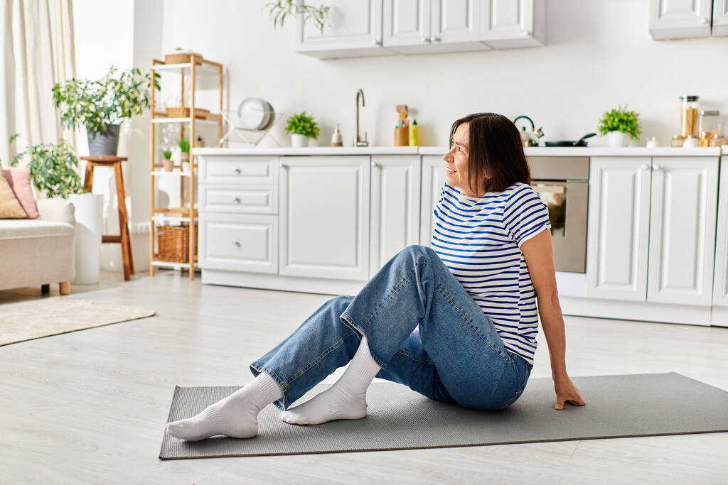 Reife Frau in gemütlicher Hausbekleidung beim Yoga auf einer Matte in ihrem Wohnzimmer. - Foto, Bild