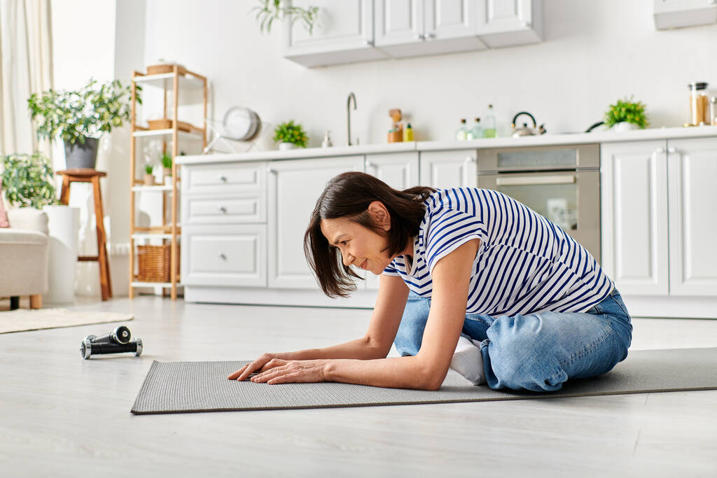Donna matura in accogliente biancheria intima si inginocchia sul tappetino yoga nel suo soggiorno. - Foto, immagini
