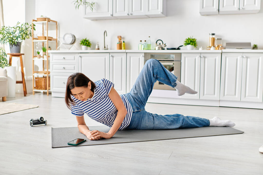 Donna matura in abbigliamento accogliente praticare yoga su un tappeto in un ambiente cucina di casa. - Foto, immagini