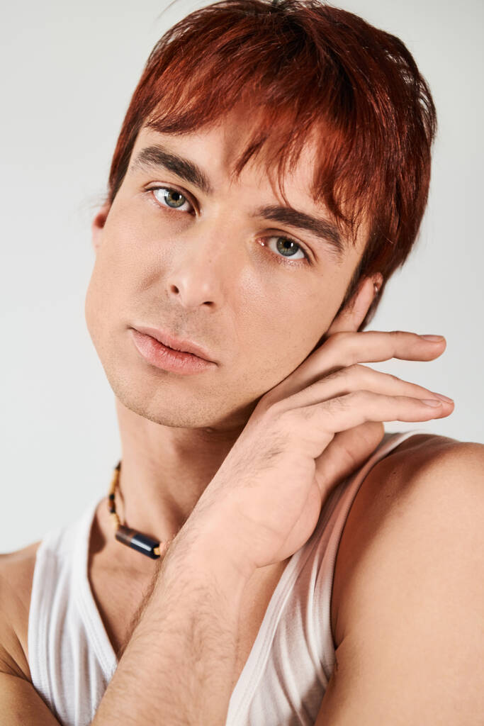 Un jeune homme élégant avec les cheveux roux frappant une pose dans un cadre studio avec un fond gris. - Photo, image