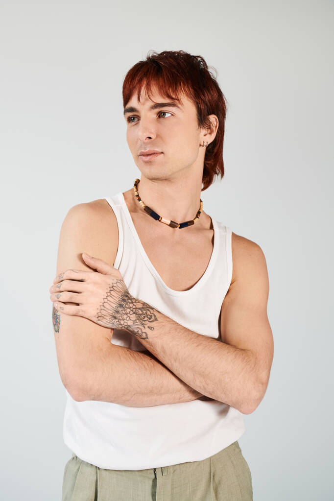 Hombre joven de moda con el pelo rojo vibrante golpea una pose en una camiseta blanca contra un fondo de estudio gris. - Foto, Imagen