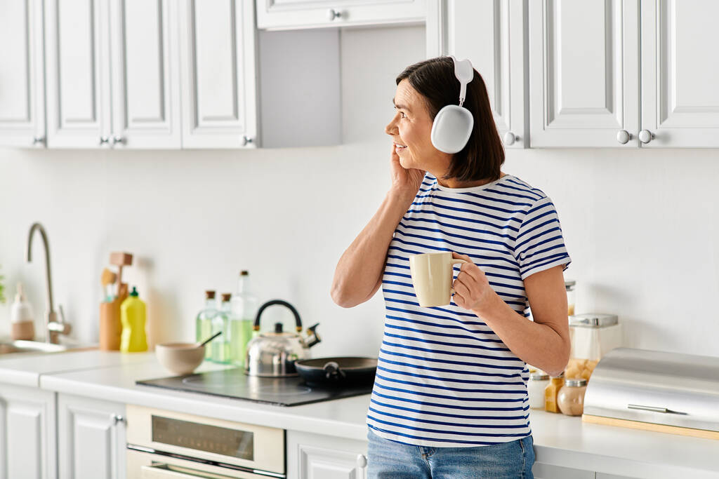 Зріла жінка в затишному домашньому вбранні насолоджується чашкою кави на кухні. - Фото, зображення