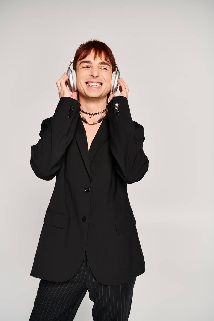 Ein stilvoller junger Mann im Anzug mit Kopfhörern vor grauem Hintergrund. - Foto, Bild