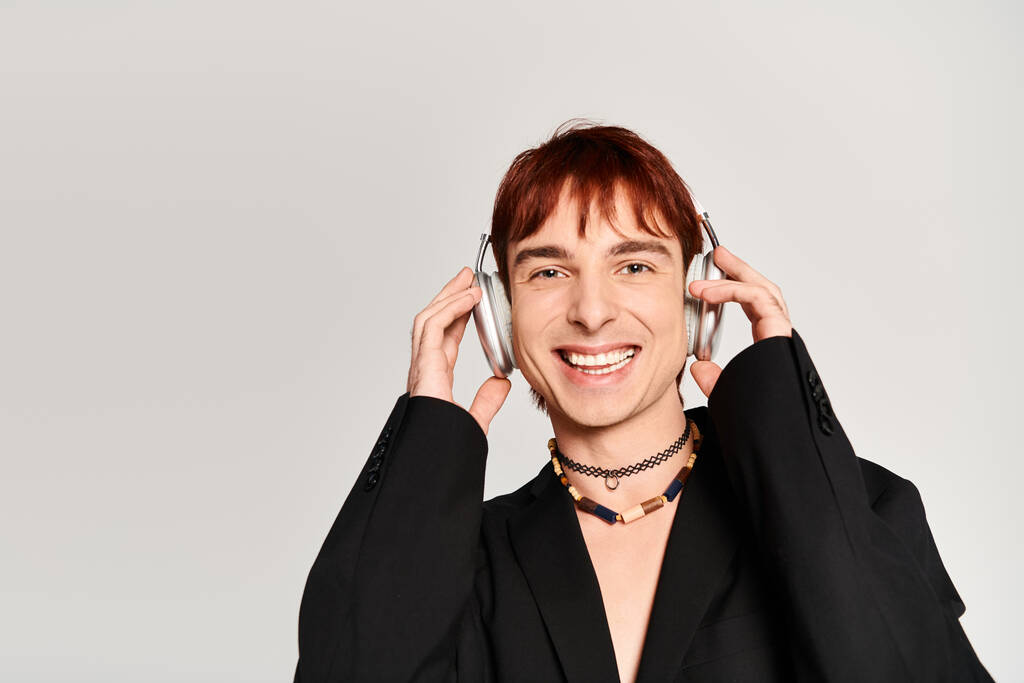 Stylový mladý muž s rudými vlasy na sluchátkách na pozadí šedého studia. - Fotografie, Obrázek