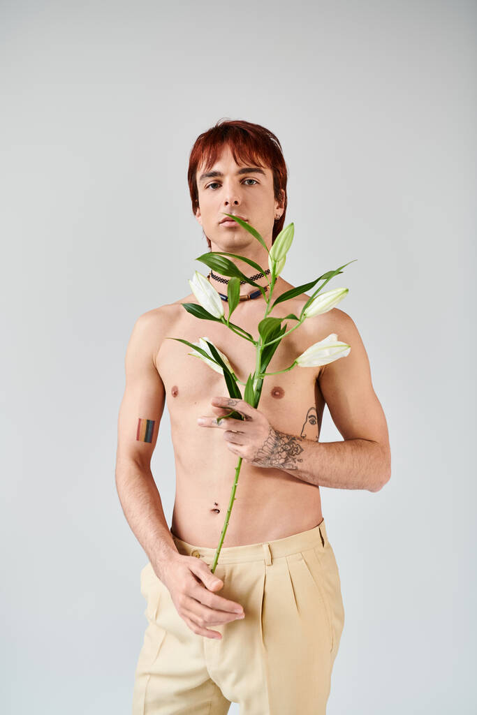 Un giovane senza camicia culla con grazia una pianta in mano, trasudando un senso di pace e connessione con la natura.. - Foto, immagini