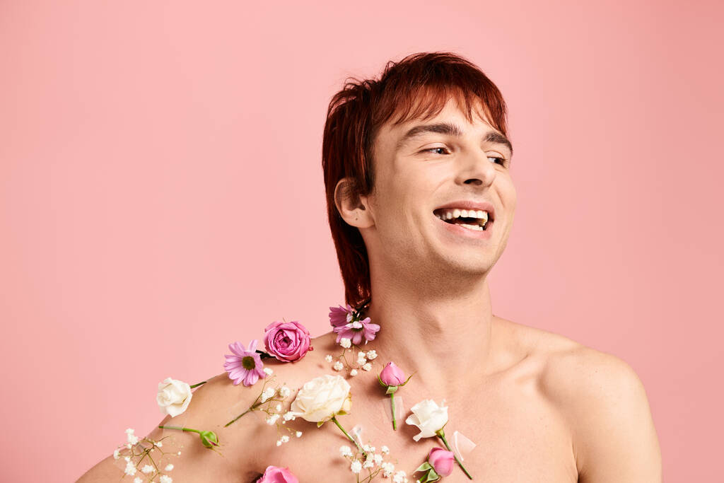 Ein junger Mann ohne Hemd zeigt in einem Atelier stolz eine Vielzahl farbenfroher Blumen, die kunstvoll auf seiner Brust arrangiert sind.. - Foto, Bild