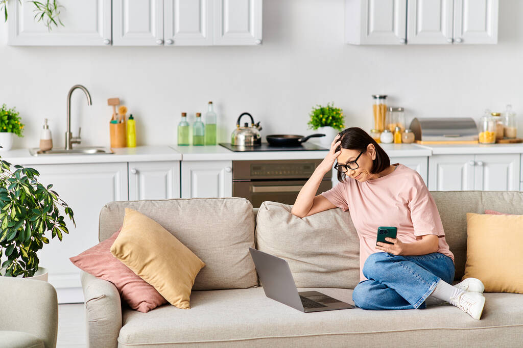 Eine Frau in bequemer Homewear sitzt auf einer Couch, in ihr Handy vertieft. - Foto, Bild