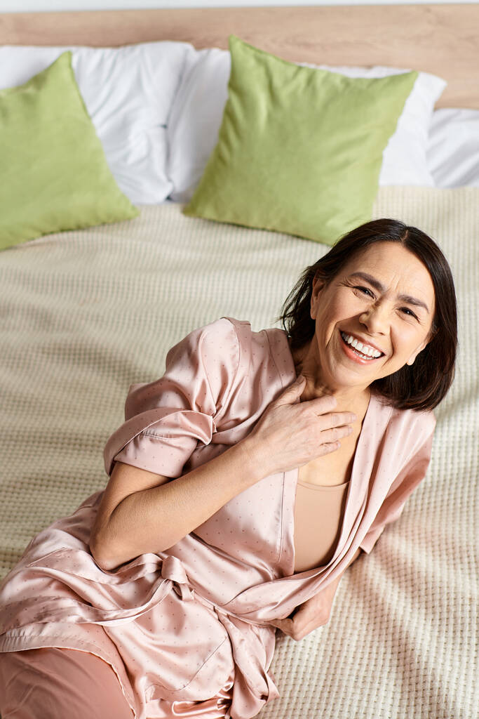 Una mujer en acogedora ropa de casa descansando en una cama rodeada de almohadas. - Foto, Imagen