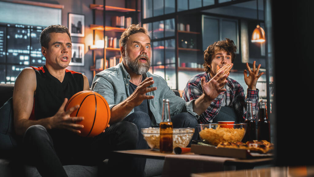 At Home Three Joyful Basketball Fanoušci sedí na gauči sledovat hru v televizi, slavit vítězství, když sportovní tým vyhraje mistrovství. Skupina přátel jásat při hraní oblíbených. - Fotografie, Obrázek
