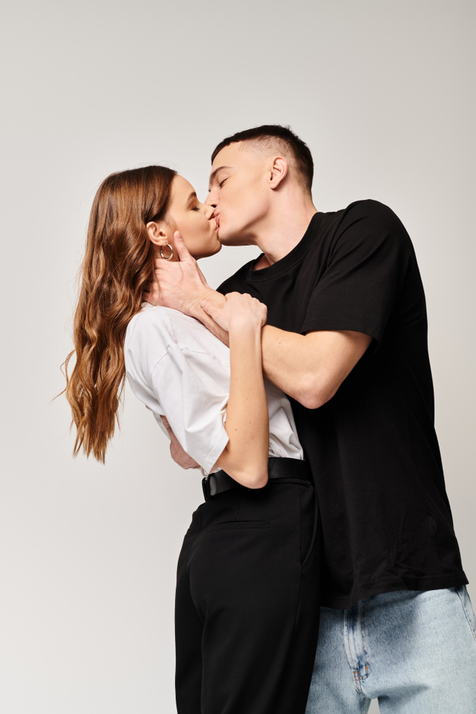 Młody mężczyzna i kobieta dzielą namiętny pocałunek w studiu z szarym tłem. - Zdjęcie, obraz