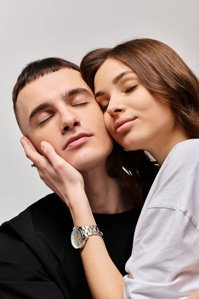 Een jong stel, man en vrouw, liefdevol omarmd in een studio met een grijze achtergrond. - Foto, afbeelding