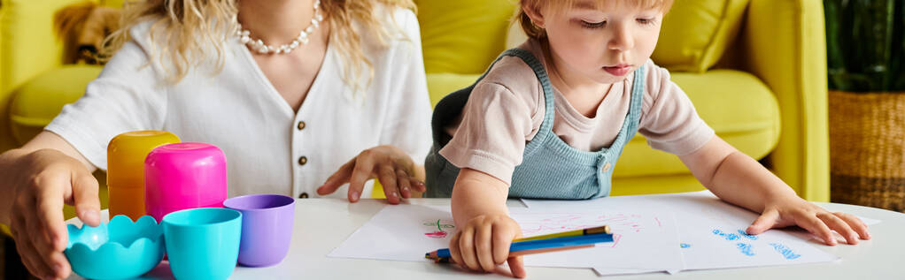 Una madre de pelo rizado y su hija pequeña se sientan en una mesa, participando en actividades de aprendizaje Montessori en un ambiente acogedor en casa. - Foto, imagen