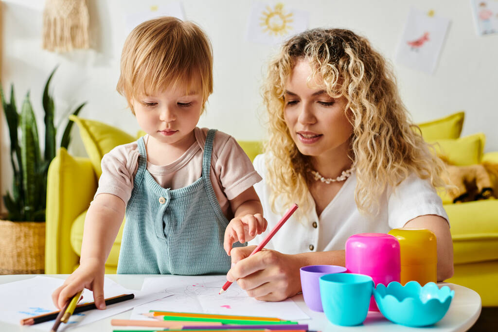 Eine Mutter mit lockigem Haar und ihre kleine Tochter sitzen an einem Tisch und üben sich zu Hause in Montessori-Pädagogik. - Foto, Bild