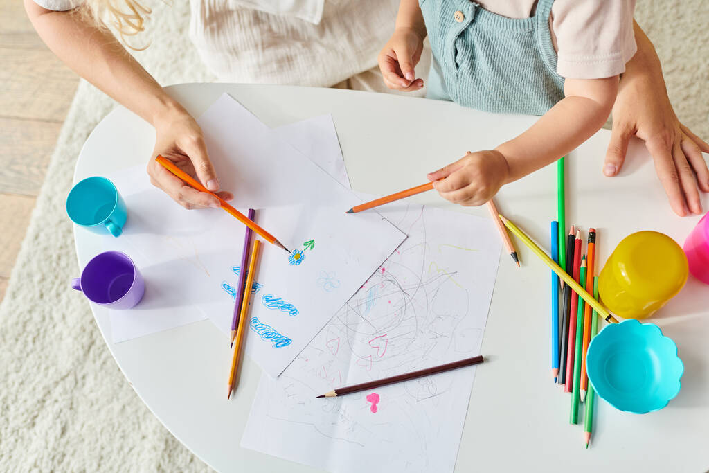bambino e mamma si siedono a un tavolo da disegno con matite colorate e pastelli. - Foto, immagini