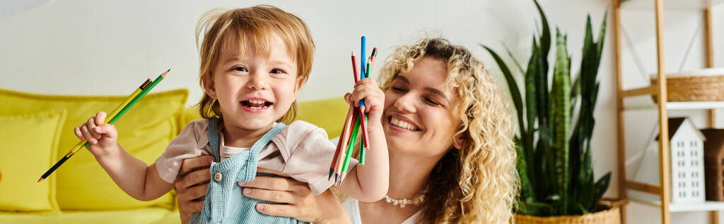 Η σγουρή μητέρα και η κόρη της κρατούν κραγιόνια, χρησιμοποιώντας τη μέθοδο Montessori. - Φωτογραφία, εικόνα