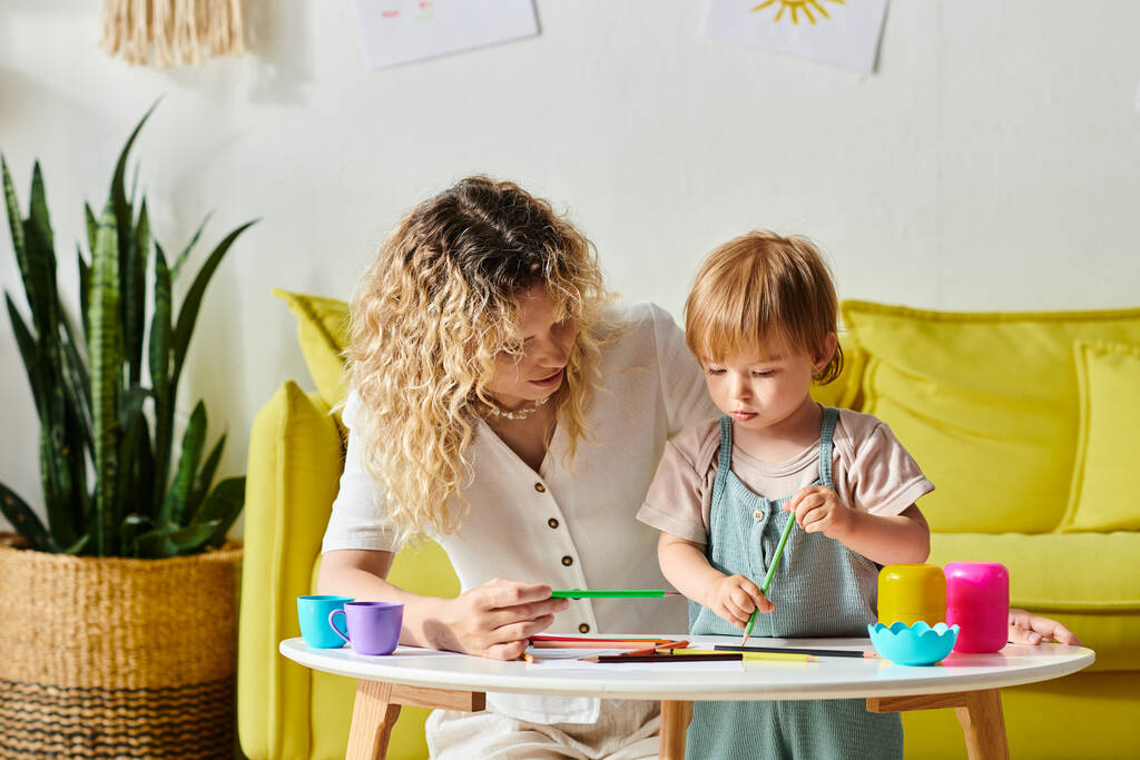 Kiharatukkainen äiti ja hänen taaperotytär harjoittavat onnellisesti Montessori-tyylistä leikkiä leluilla kotona. - Valokuva, kuva