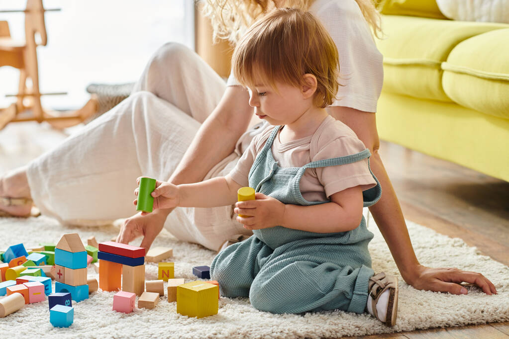 Egy göndör anya és kislánya gyakorlatias tanulást folytat a padlón lévő tömbökkel, a Montessori-módszert alkalmazva.. - Fotó, kép