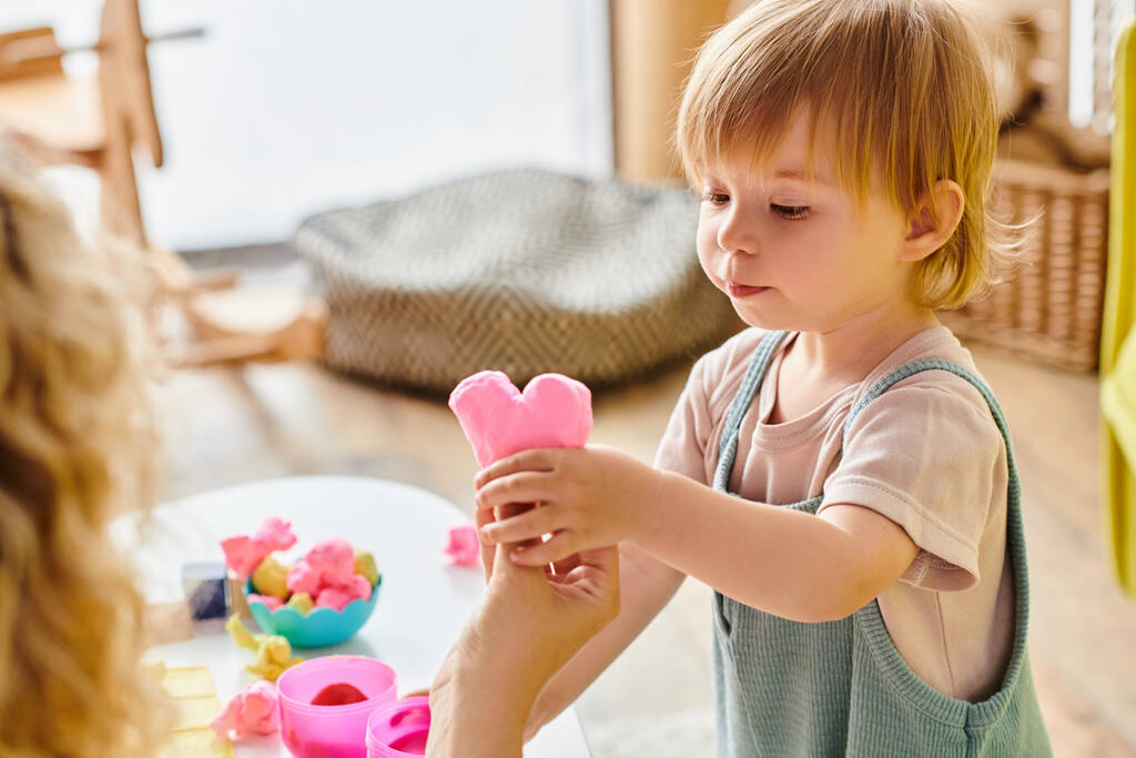 Μια σγουρή μητέρα δίνει δύναμη στην κόρη της στο Μοντεσόρι να παίξει με ένα πολύχρωμο, εκπαιδευτικό παιχνίδι.. - Φωτογραφία, εικόνα