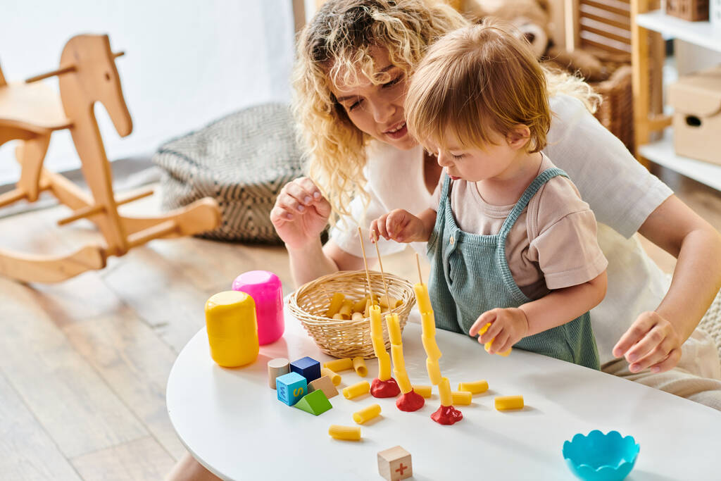 Μια σγουρή μητέρα και η κόρη της ασχολούνται με το έργο Montessori, εξερευνώντας παιχνίδια και μαθαίνοντας μαζί στο σπίτι. - Φωτογραφία, εικόνα