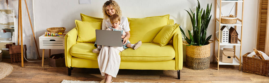 Nainen, jolla on kiharat hiukset, istuu keltaisella sohvalla, keskittyen kannettavaan tietokoneeseen.. - Valokuva, kuva