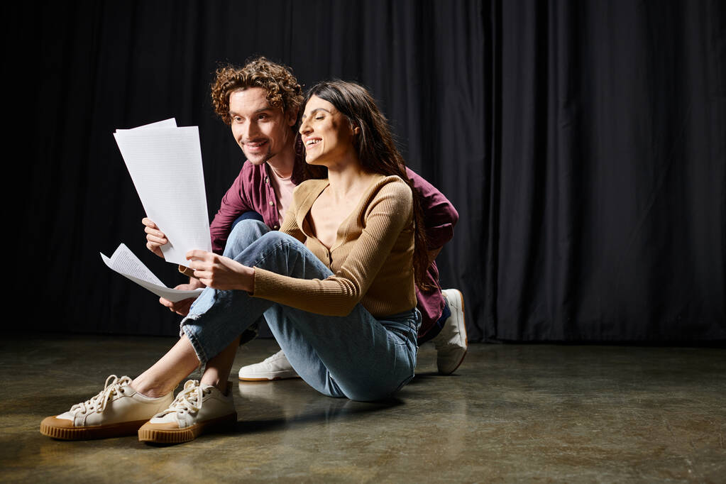 Uomo e donna seduti sul pavimento, che tengono documenti, discutono di sceneggiature teatrali. - Foto, immagini