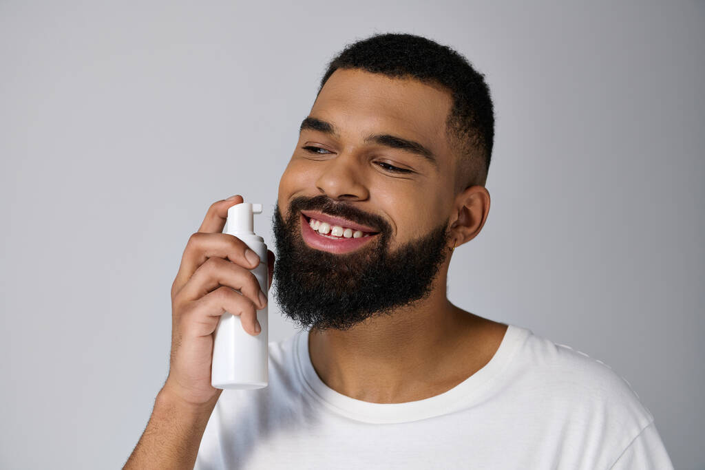 Hombre afroamericano joven y guapo con barba sosteniendo un tubo de loción. - Foto, imagen