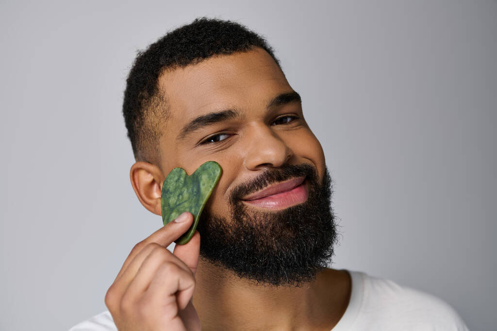 African american young man holds gua sha for skincare routine. - Photo, Image