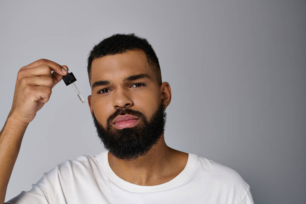 African american attractive young man with a beard holding a bottle of serum. - Photo, Image