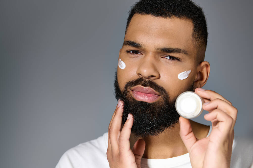 Africain américain attrayant jeune homme qui applique de la crème sur son visage. - Photo, image