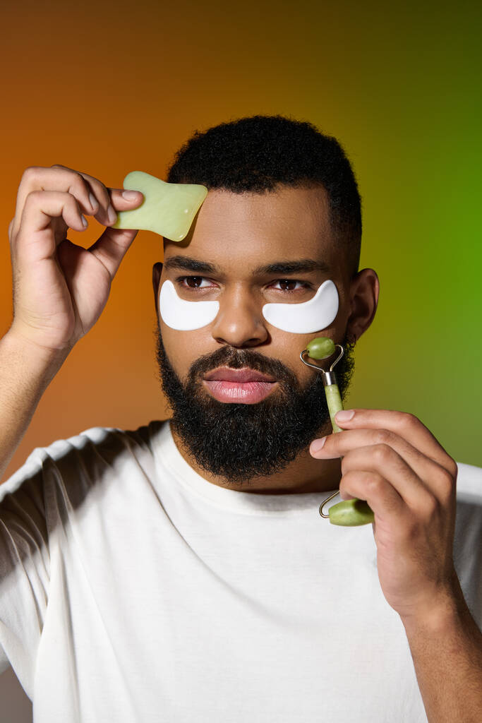 Homme barbu afro-américain utilisant des patchs pour les yeux et un rouleau de visage. - Photo, image